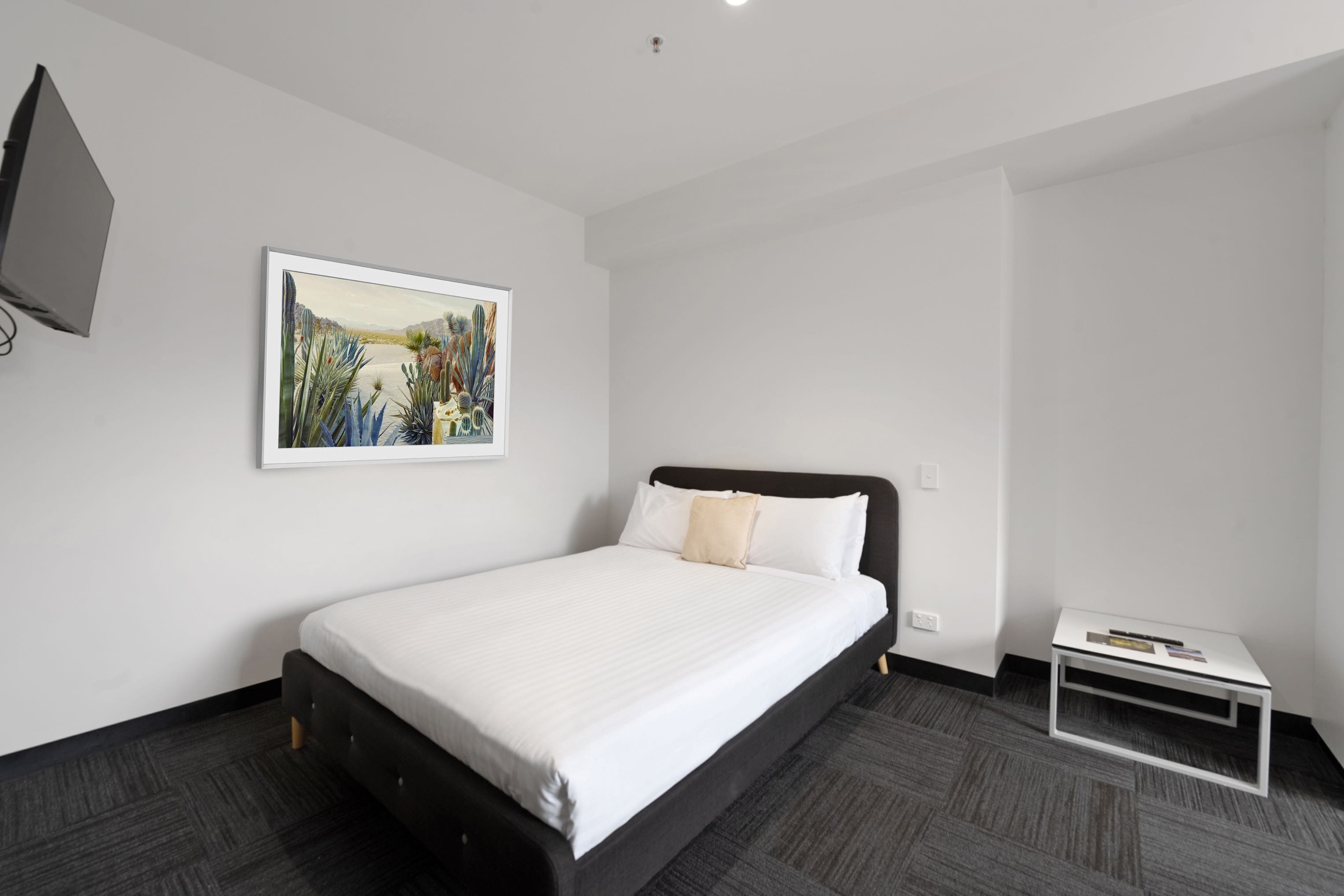 A modern hotel room with a large bed, a small bedside table, and a painting on the wall.