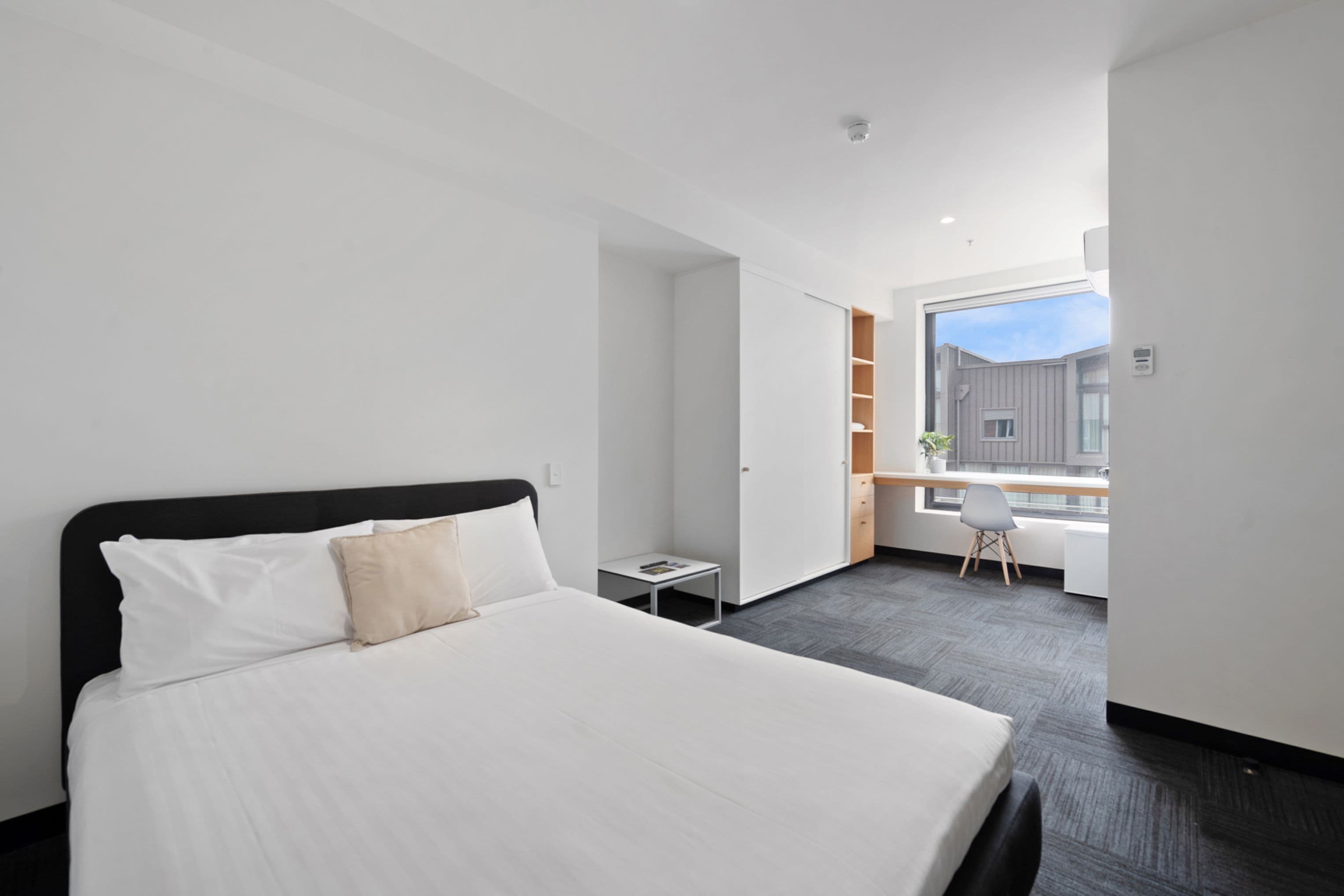 Habitación de hotel moderna con una cama grande, un escritorio pequeño y una ventana con vistas a la ciudad.