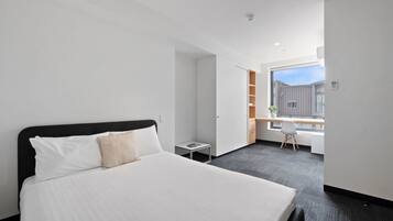 Habitación de hotel moderna con una cama grande, un escritorio pequeño y una ventana con vistas a la ciudad.