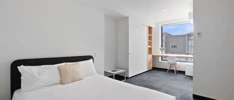 Habitación de hotel moderna con una cama grande, un escritorio pequeño y una ventana con vistas a la ciudad.