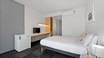 Una habitación de hotel moderna con cama, escritorio, televisor y un refrigerador pequeño.