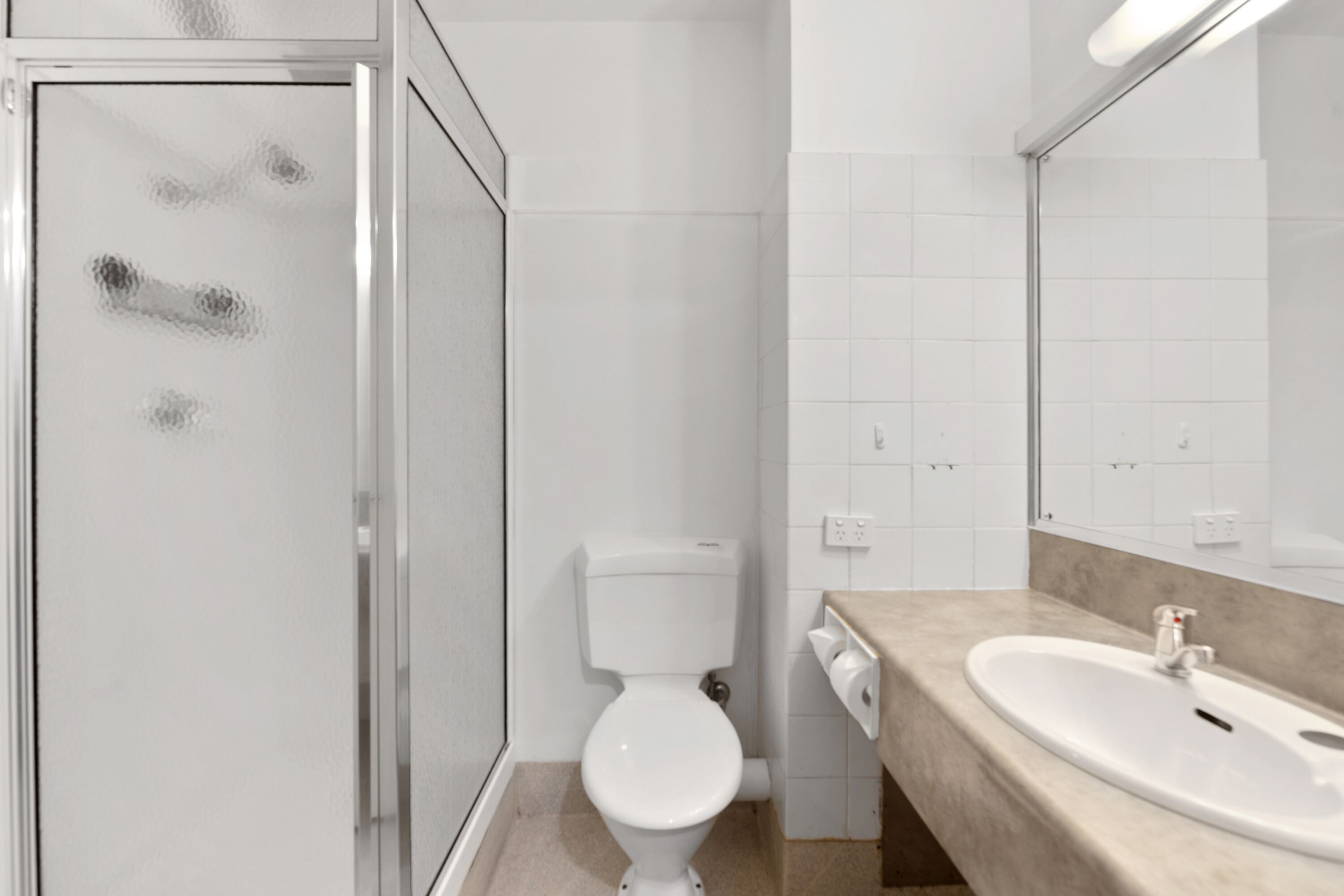 Un bagno con box doccia in vetro, un water bianco e un lavabo beige con uno specchio soprastante.