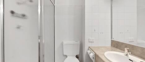 Un bagno con box doccia in vetro, un water bianco e un lavabo beige con uno specchio soprastante.