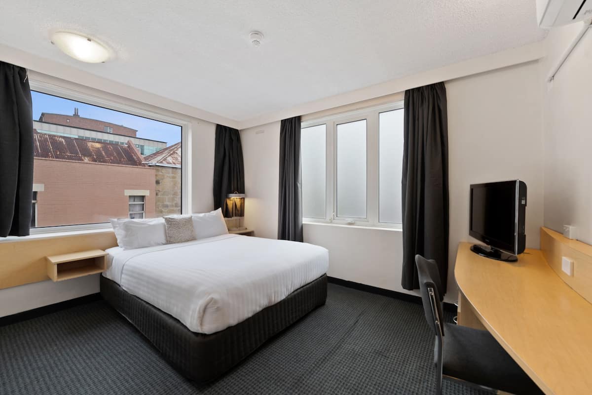 A hotel room with a large bed, a desk, a TV, and a window with curtains.