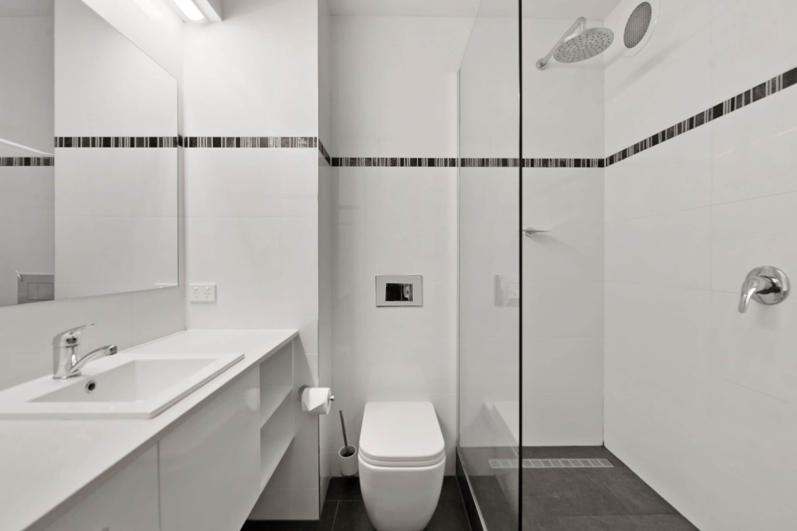 Un baño moderno con lavamanos, inodoro y zona de ducha blancos.