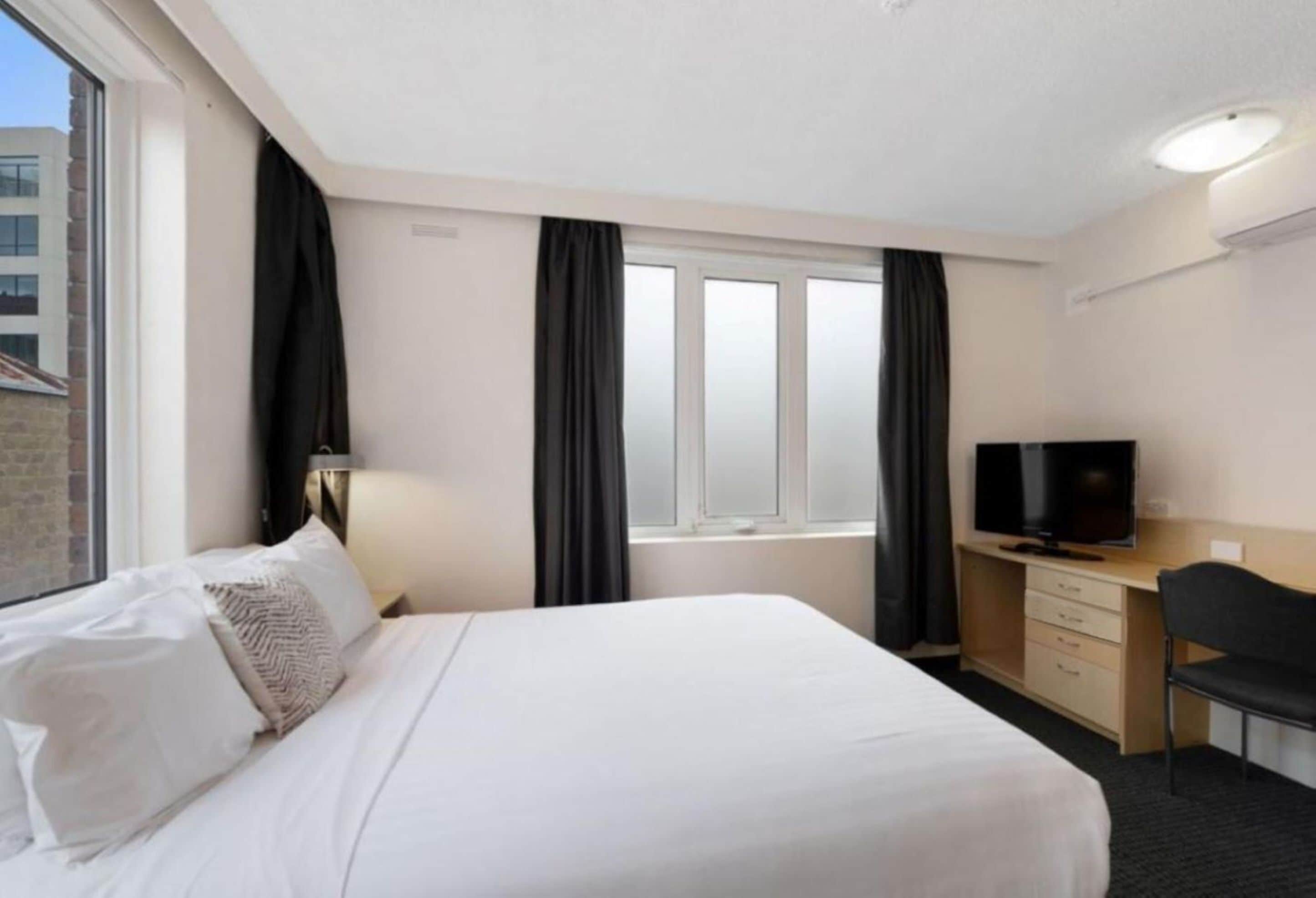 Habitación de hotel con cama, escritorio con televisor y ventana con cortinas.
