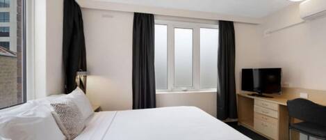Habitación de hotel con cama, escritorio con televisor y ventana con cortinas.