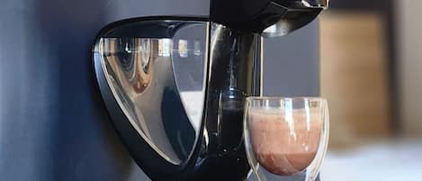 A coffee machine with a cup of coffee, a plate of macarons, and a coffee grinder on a countertop.