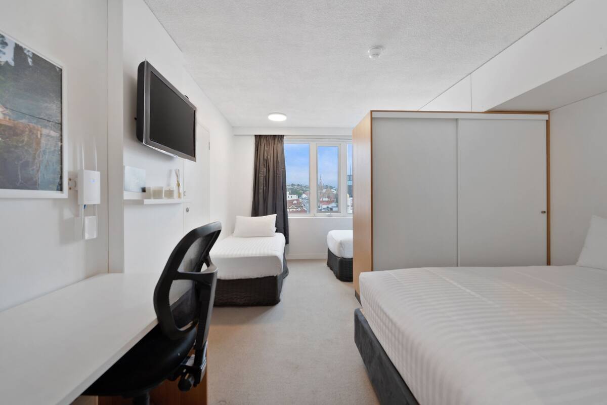 A hotel room with a bed, a desk, a chair, a TV, and a wardrobe.