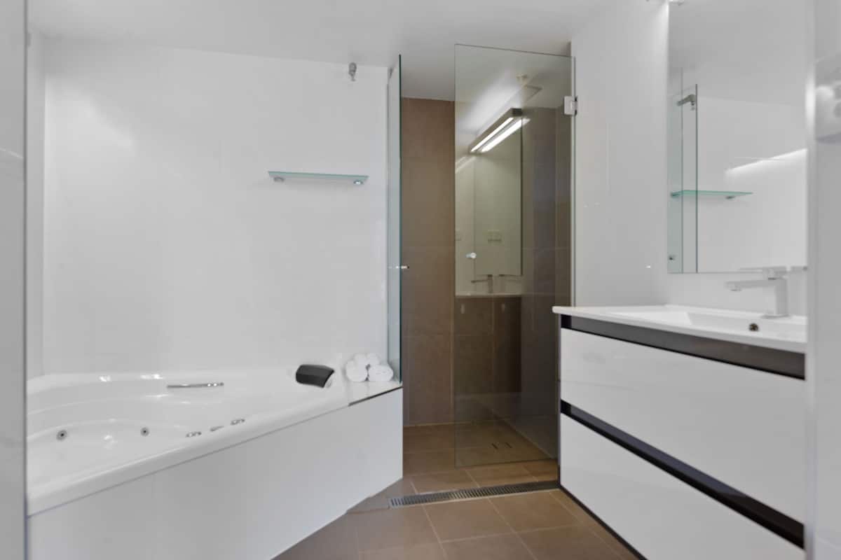 A modern bathroom with a white bathtub, a glass shower enclosure, and a white vanity with a mirror.