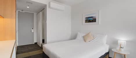 A hotel room with a bed, bedside table, and a painting on the wall.