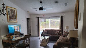 A living room with a sofa, a coffee table, a TV, a dining table with chairs, and a ceiling fan. - Private Pool Home Near the Parks (Davenport)