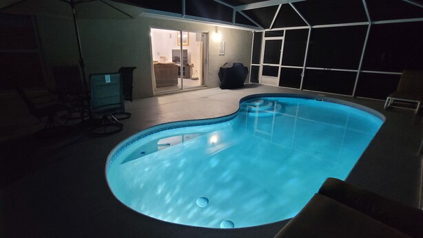 A swimming pool with a curved edge, a covered patio area, and a door leading to an interior space. - Private Pool Home Near the Parks (Davenport)