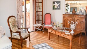 A traditional room with a wooden floor, a wooden dining table, a red upholstered chair, a white armchair, and a wooden cabinet with decorative items. - Stunning home in Bergerac (Bergerac)
