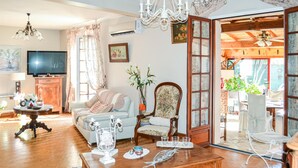A cozy living room with a sofa, a wooden coffee table, a TV, and a dining area with chairs and a table. - Stunning home in Bergerac (Bergerac)