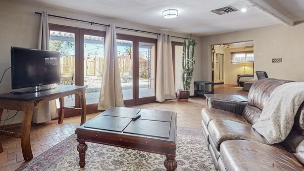 Una sala de estar con televisor, sofá, mesa de centro y un ventanal con cortinas.