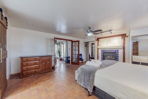 A bedroom with a bed, a dresser, a ceiling fan, a fireplace, and a door leading to another room.