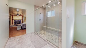 Un baño moderno con cabina de ducha de vidrio, suelo de baldosas y una chimenea visible en la habitación contigua.
