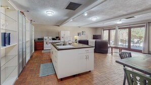 Cocina compacta con gabinetes blancos, una isla central y un comedor con mesa y sillas.