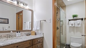 A bathroom with a marble countertop, wooden vanity, a glass shower enclosure, and a toilet. - Outpost: Yampa 2424 - Aspens Location! (Wilson)