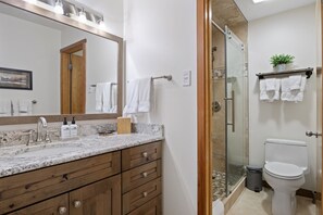 Een badkamer met een marmeren aanrechtblad, een houten wastafelmeubel, een douchecabine van glas en een toilet.