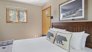 A bedroom with a bed, two pillows with bear designs, a nightstand with a lamp, a framed picture on the wall, and a window with a view of trees. - Outpost: Yampa 2424 - Aspens Location! (Wilson)