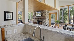 A kitchen with a stone fireplace, wooden beams, and a large window overlooking a deck. - Outpost: Yampa 2424 - Aspens Location! (Wilson)