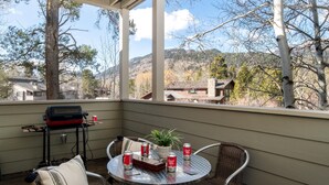 Un patio techado con una mesa redonda, sillas de mimbre, una parrilla y vistas a un paisaje montañoso.