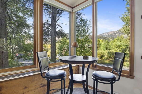 A corner room with a large window, two chairs, and a small table.