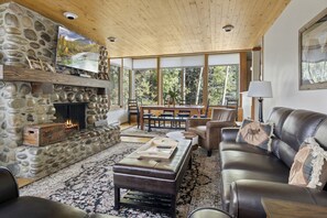 A stone fireplace with a television above it, a leather sofa, and a dining area with a table and chairs.