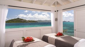 Una habitación con dos camas, vista al mar y una isla distante, y una ventana con cortinas blancas.