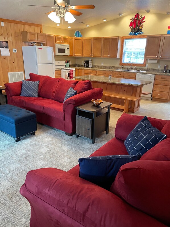 Cocina moderna con armarios de madera, una isla central y un comedor con sofá y reposapiés rojos.