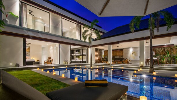 A modern pool area with a glass-enclosed pool, lounge seating, and ambient lighting. - Villa Waha (Canggu)
