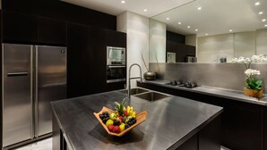 A modern kitchen with a stainless steel refrigerator, oven, and sink. A wooden fruit bowl is placed on the countertop. - Villa Waha (Canggu)