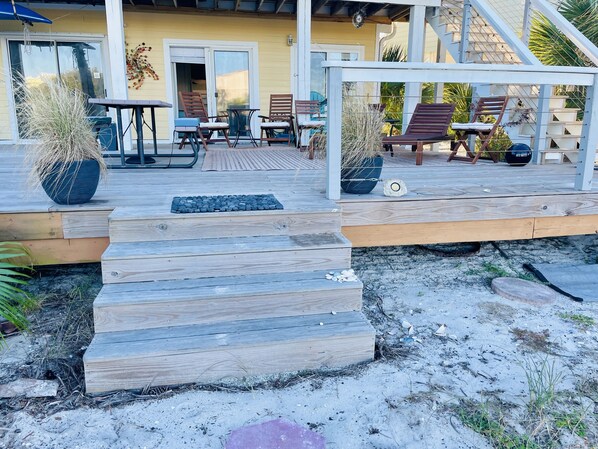 Una terraza de madera con mobiliario exterior, una planta en maceta y una escalera que lleva a un porche cubierto.