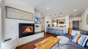 A modern living room with a fireplace, a bar area, and a kitchen in the background. - Welcome to Mountain Dreams + River Streams! (Silverthorne)