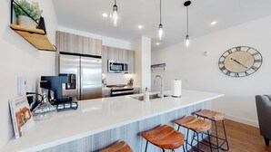 A modern kitchen with a central island, stainless steel appliances, and wooden bar stools. - Welcome to Mountain Dreams + River Streams! (Silverthorne)