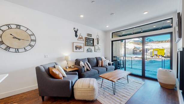 A modern living room with a large wall clock, a sofa set, a coffee table, and a view of a snowy landscape through large glass doors. - Welcome to Mountain Dreams + River Streams! (Silverthorne)