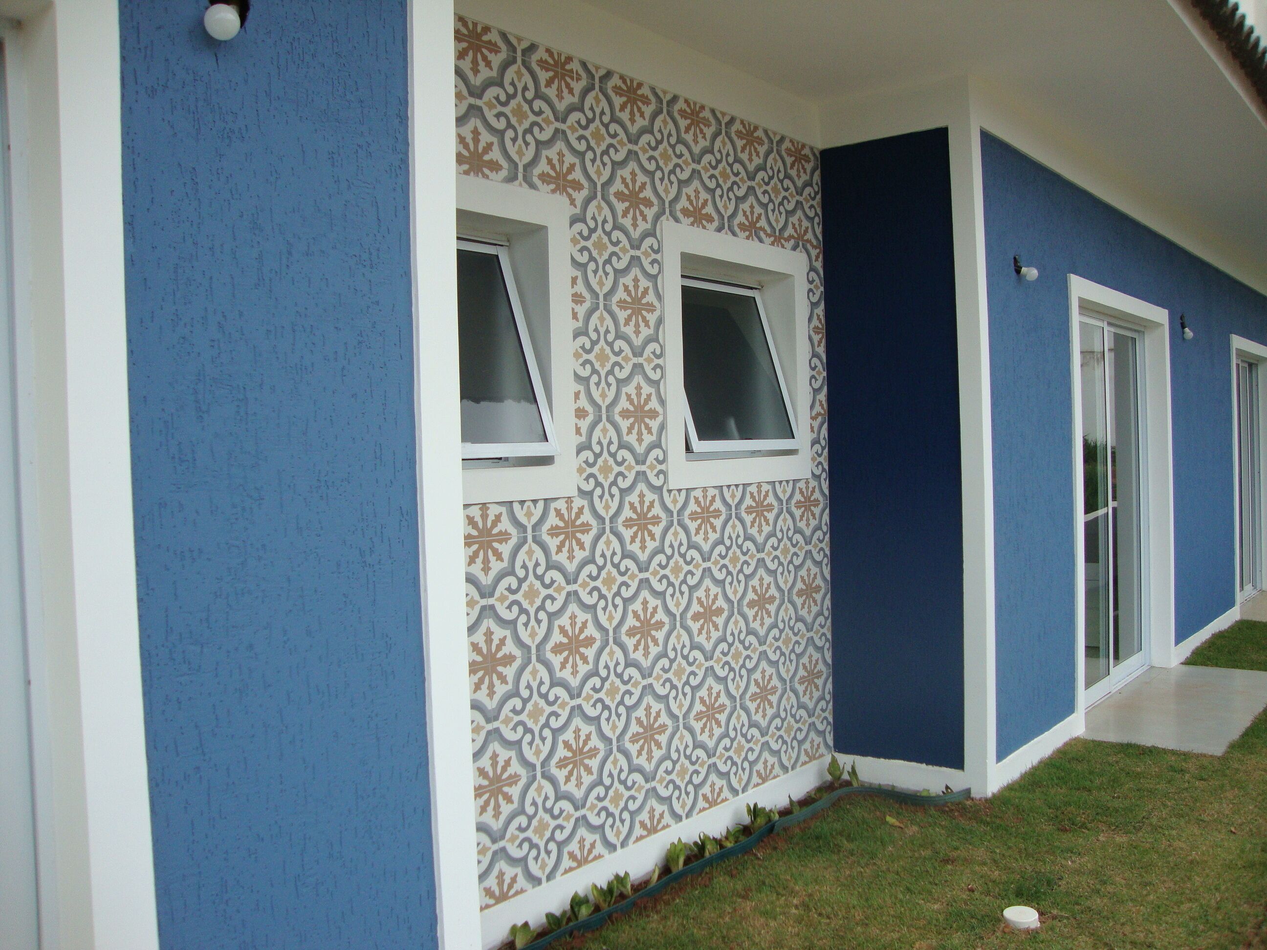 Ein Gebäude mit blauer Fassade, gemusterten Wandfliesen und zwei Fenstern mit weißen Rahmen.