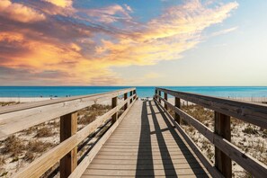 A wooden boardwalk leading to a beach with clear skies and a sunset. - Emerald Shores: Steps from the Gulf, Navarre Beach (Navarre)