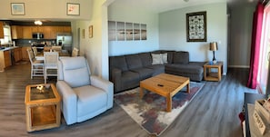 A modern living room with a sofa, armchair, coffee table, and a dining area with chairs.