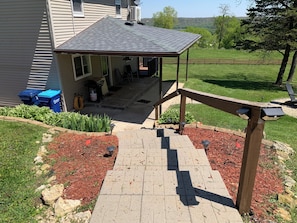 A covered patio area with a brick pathway leading to a house.