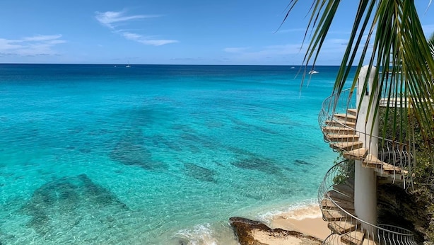 Un mar turquesa cristalino con una escalera que baja a una playa, rodeada de palmeras.