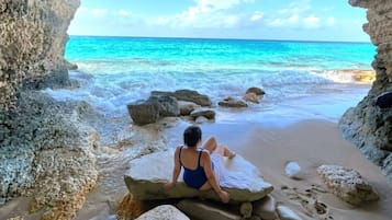 Una persona sentada sobre rocas en una playa, con vista despejada del océano a través de una abertura parecida a una cueva.