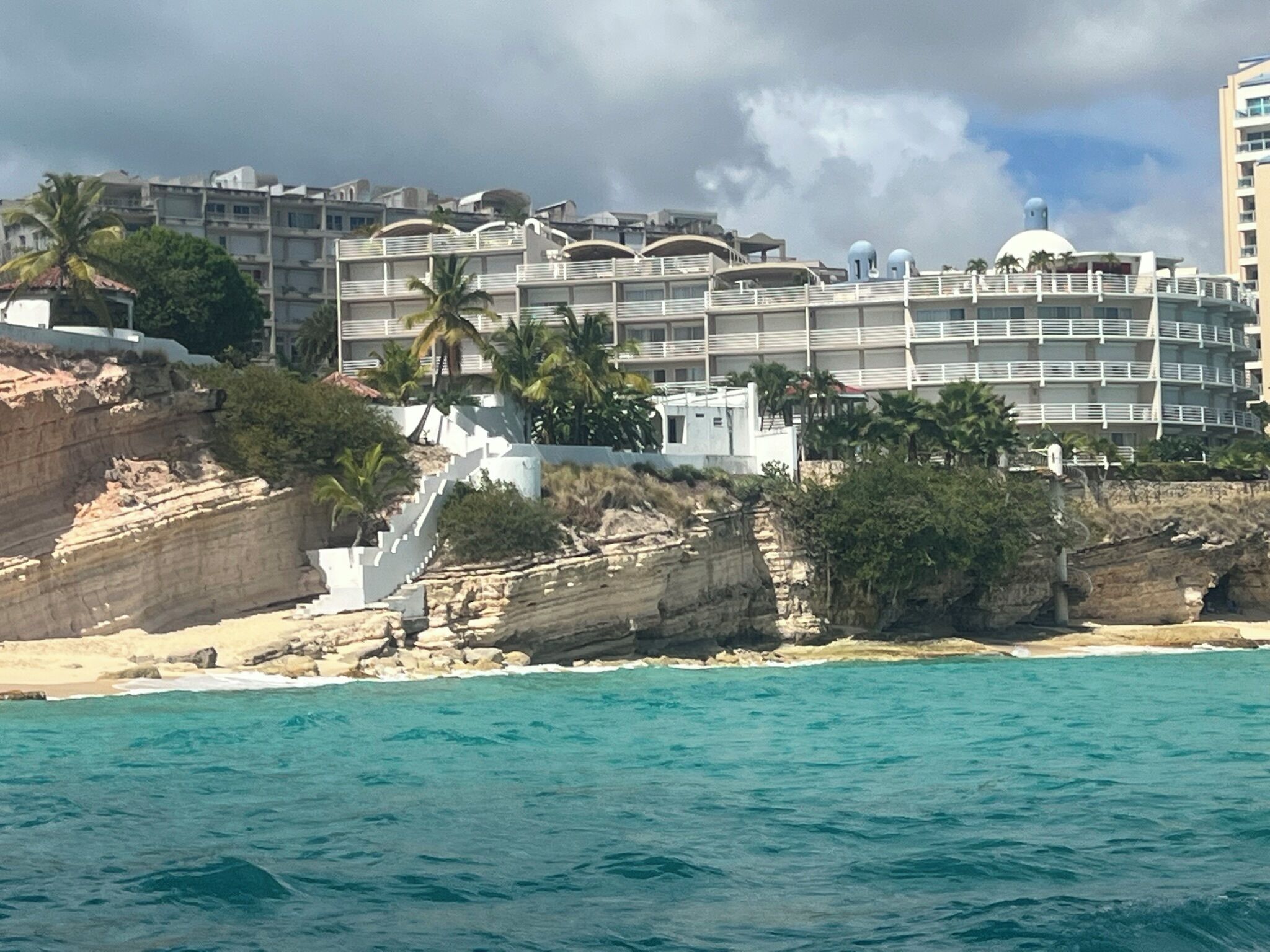 A coastal hotel with multiple balconies, a beach view, and a rocky shoreline.