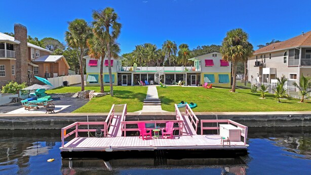 A dock with a boat, a pool, and a building with a green roof and white walls. - The Mermaid Studio (New Port Richey)