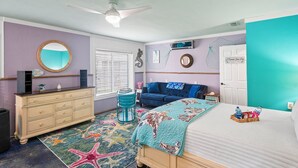 A bedroom with a bed, dresser, and a blue chair. - The Mermaid Studio (New Port Richey)