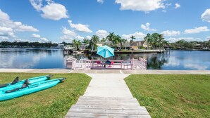 A dock leading to a waterfront area with kayaks and a blue umbrella. - The Mermaid Studio (New Port Richey)