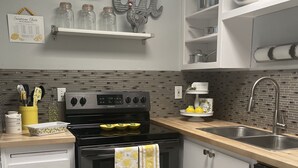 Una cocina moderna con una estufa negra, ollas de acero inoxidable, un fregadero y un armario blanco con una toalla amarilla.
