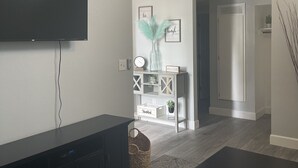Una sala de estar moderna con una televisión de pantalla plana, muebles oscuros, un tapete estampado y un mueble de consola decorativo con un florero y arte de pared.